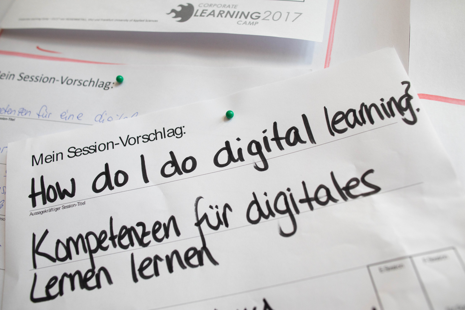 Sessionvorschlag auf dem #CLC17 (Foto von Frank Rumpenhorst), Auf dem Bild ist ein Zettel mit einem Session-Vorschlag im Rahmen des Corporate Learning Camps 2017 zu sehen. Oben steht: „Mein Session-Vorschlag:" Darunter auf Englisch: „How do I do digital learning?" Und auf Deutsch: „Kompetenzen für digitales Lernen lernen" Der Zettel ist mit einer grünen Pinnnadel an einer Wand oder Pinnwand befestigt. Im Hintergrund sind weitere Zettel sichtbar.
