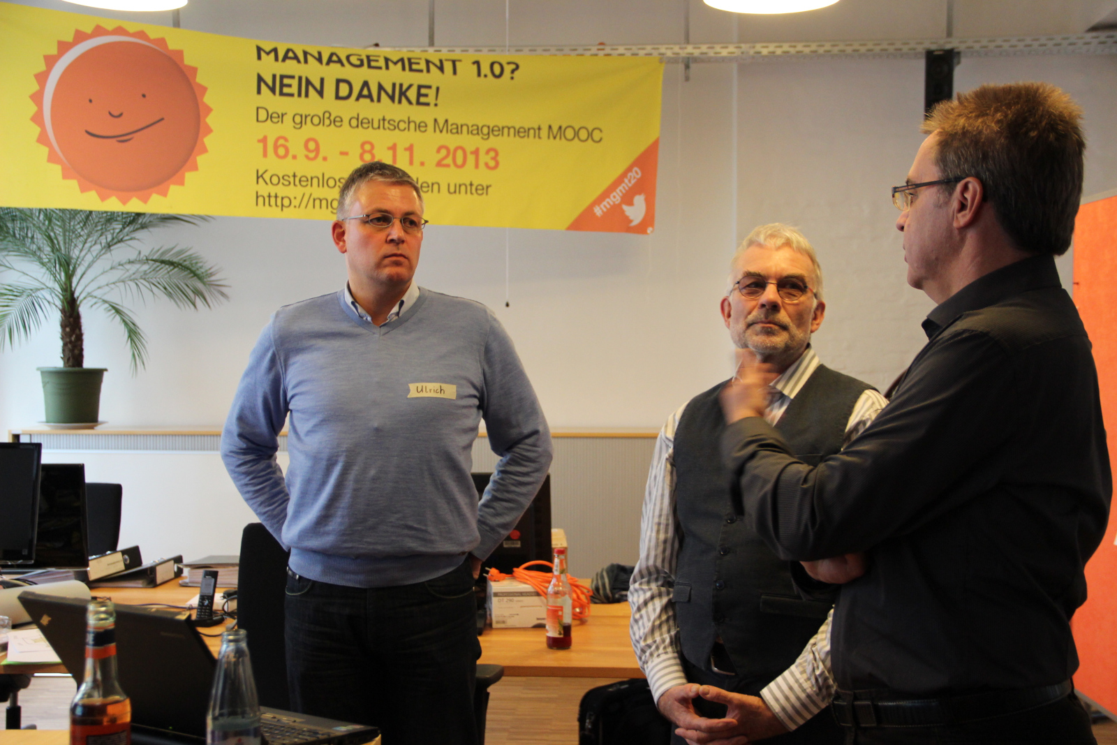 Karlheinz beim 19. Knowledge Jam (ckj19) im November 2013\
in der Cogneon Akademie (Quelle: Simon Dückert), Auf dem Bild stehen drei Männer in einem Raum und sprechen
miteinander. Einer von ihnen erklärt gerade etwas mit Handbewegungen. Im
Hintergrund hängt ein gelbes Plakat mit der Aufschrift: \"MANAGEMENT
1.0? NEIN DANKE! Der große deutsche Management MOOC 16.9. --
8.11.2013\"