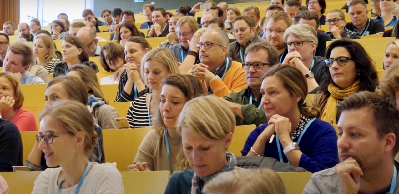 Auf dem Bild sitzen viele Menschen in einem Hörsaal. Sie schauen nach
vorn und hören aufmerksam zu. Einige machen sich Notizen oder denken
nach. Die Stimmung ist ruhig und konzentriert. Es sieht aus wie eine
Vorlesung, ein Vortrag oder eine
Konferenz.
