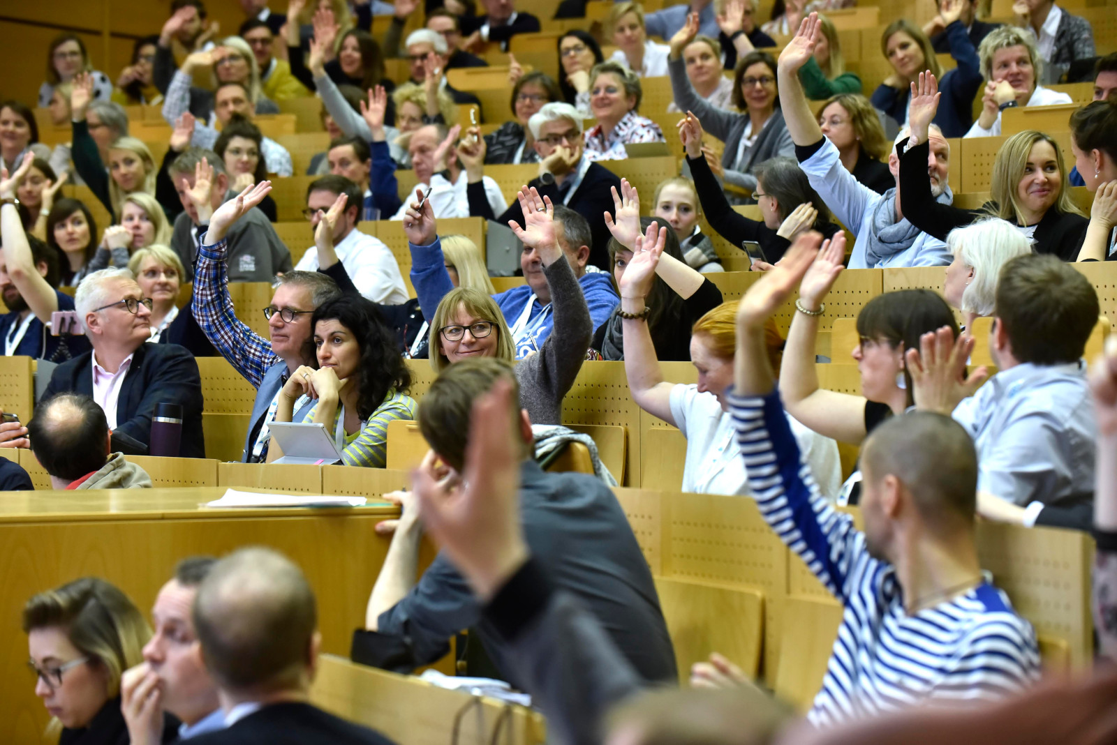 Interessensbekundungen zu Sessionvorschlägen auf dem #CLC19HH (Foto von Christian Augustin, im Auftrag von Nordmetall, CC BY 4.0), Auf dem Bild sitzen viele Menschen in einem großen Raum, ähnlich wie in einem Hörsaal. Viele von ihnen heben eine Hand. Sie zeigen damit ihr Interesse an einer vorgeschlagenen Session an. Die Menschen wirken aufmerksam und beteiligt.