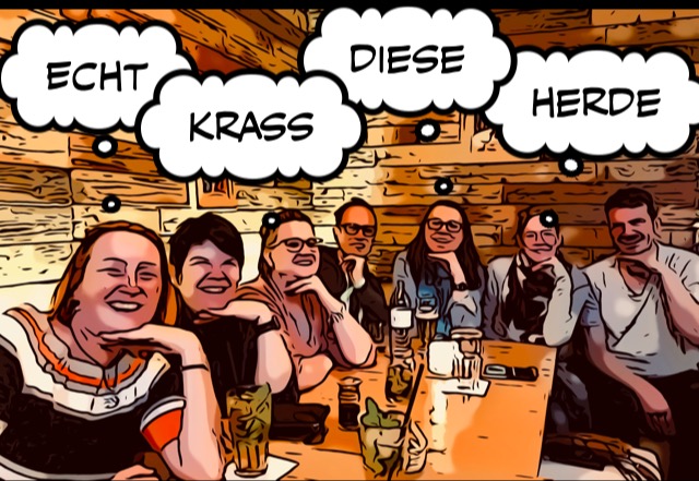 Die Grafik zeigt eine Comic-Zeichnung von acht Personen, die fröhlich
an einem Tisch in einer Hütte sitzen. Alle lachen oder lächeln. Über
ihren Köpfen stehen in Sprechblasen die Wörter: „Echt -- krass -- diese
-- Herde".